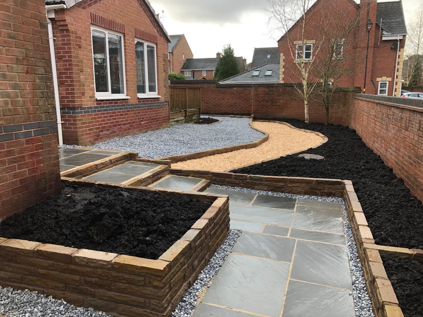 Finished low-maintenance garden in Grappenhall with slate chippings, a curved gravel path, raised brick planting beds and a retained silver birch
