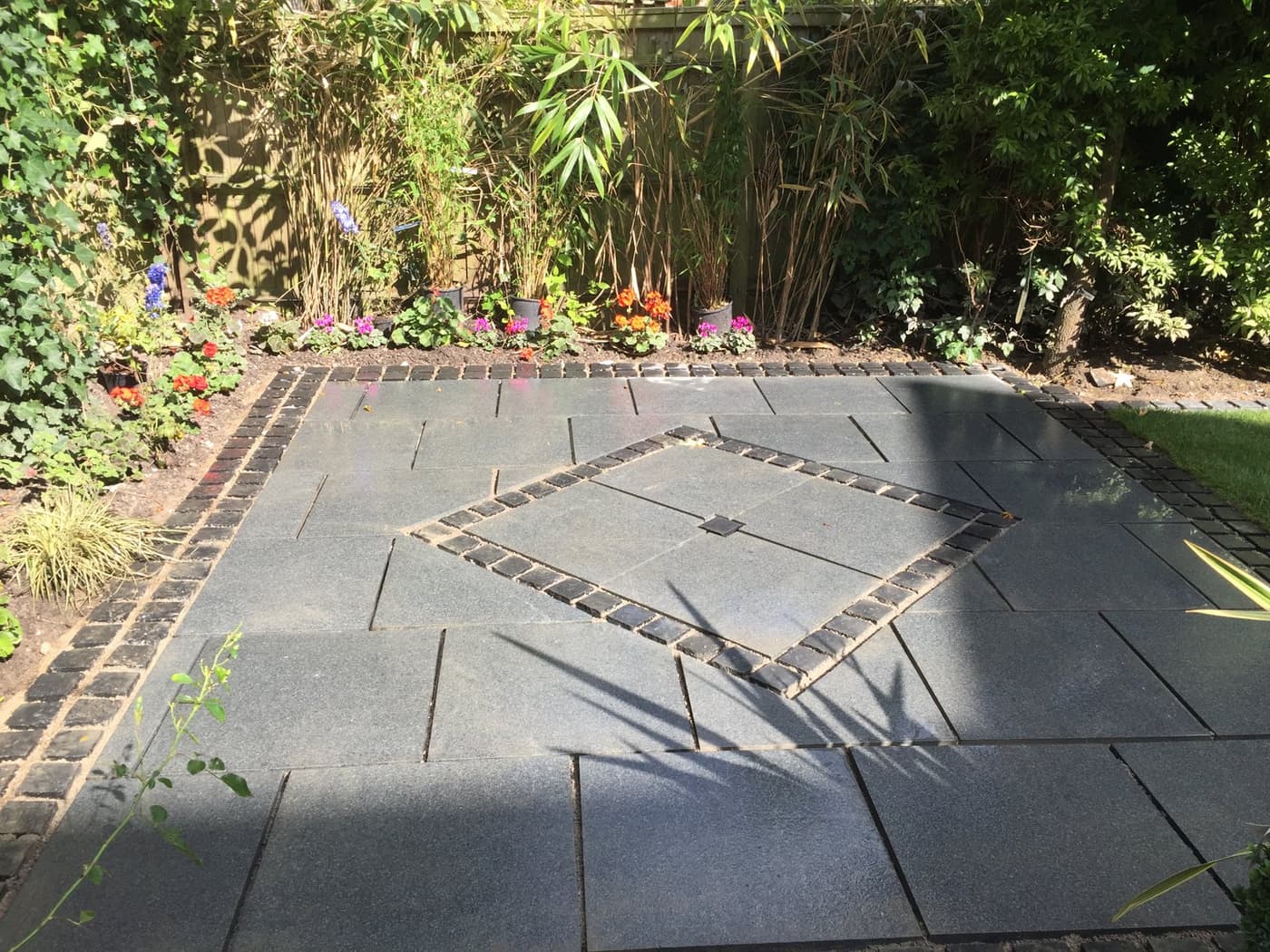 Flamed granite patio with a diamond-set feature panel and black granite sett border in a walled Cheshire garden