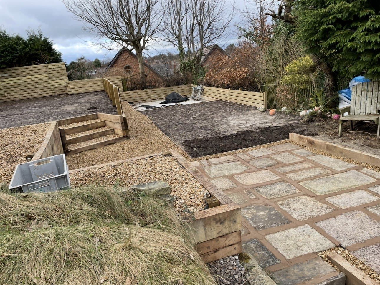 Steep garden re-engineered into level terraces with oak sleepers, cobble-edged paving and gravel steps
