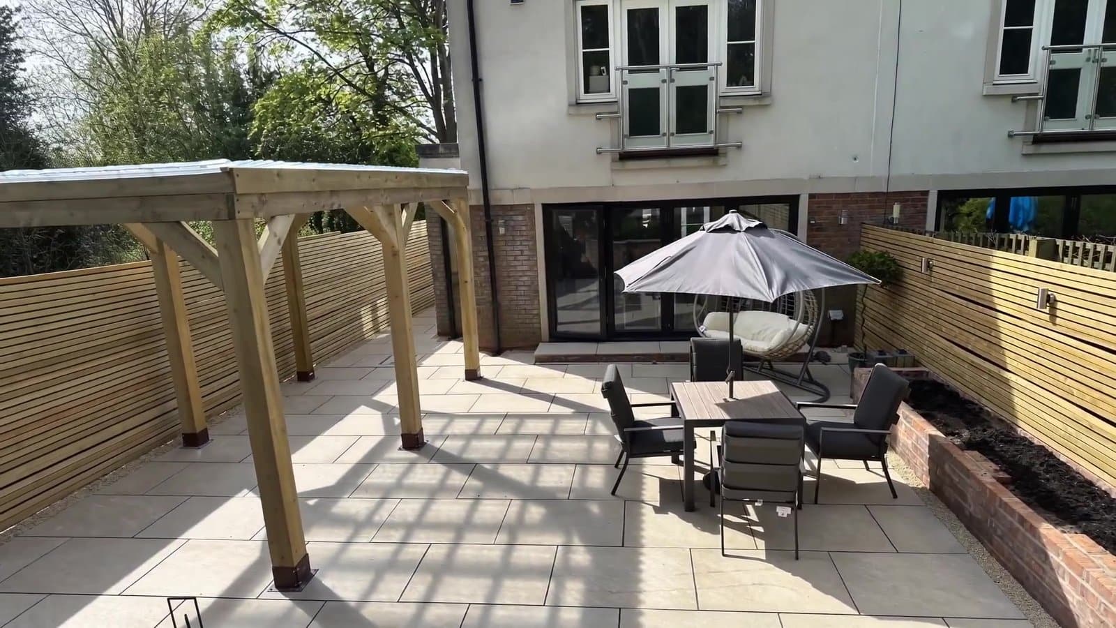 Completed outdoor living space in Cheshire: large-format porcelain patio with an oak pergola and slatted fencing