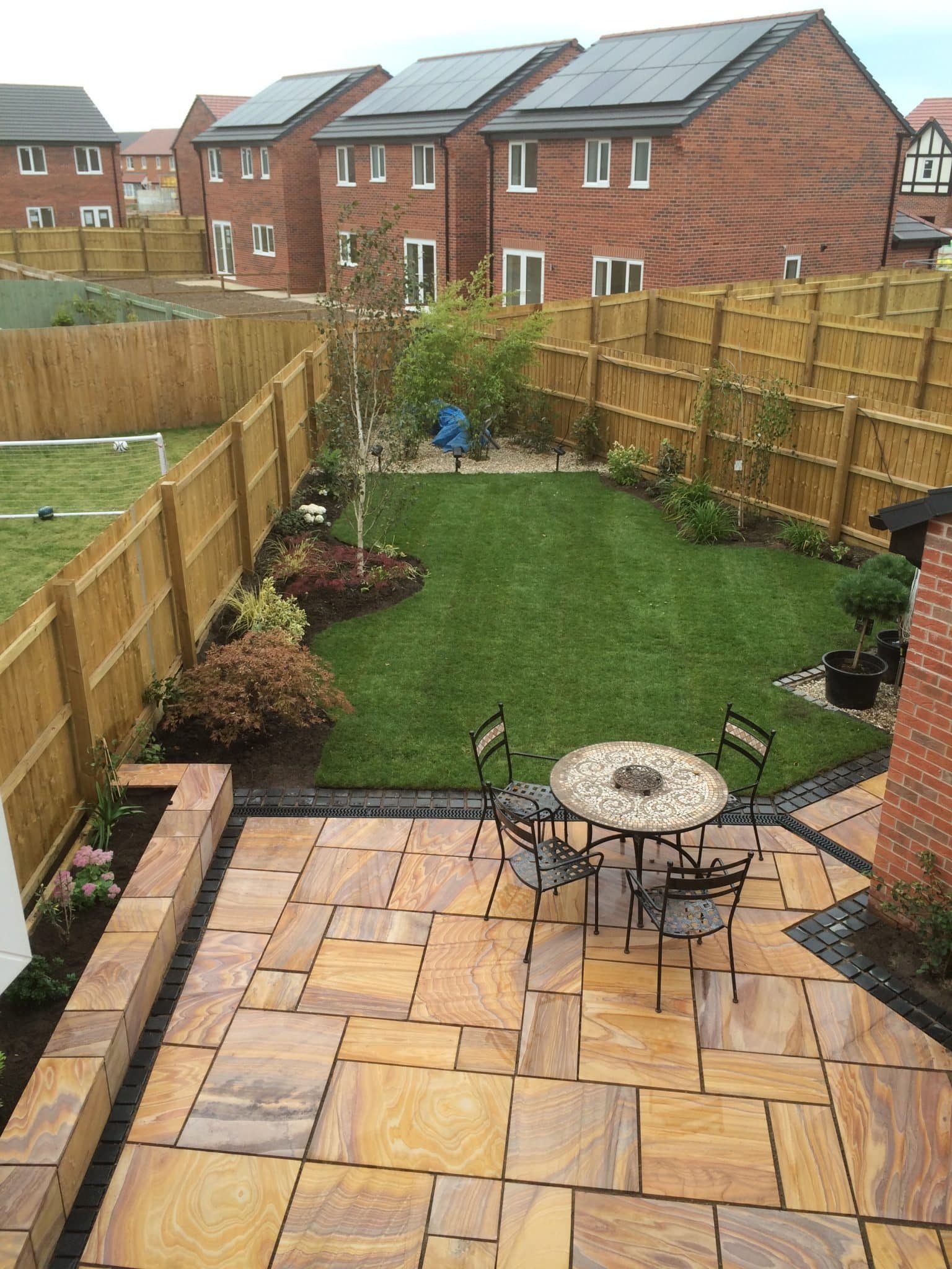 Rainbow sandstone patio with a curved new lawn and planted borders in a Cheshire garden