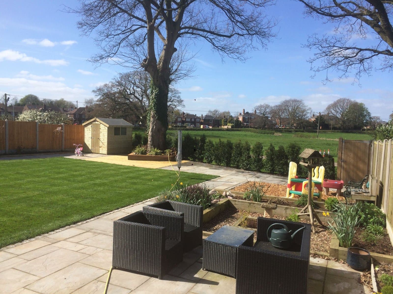 Family garden after a full makeover: new lawn, patio and hedging opening onto fields